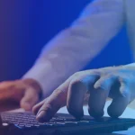 Close-up of a person typing on a laptop with a blue gradient overlay and the B EYE logo in the top-right corner.